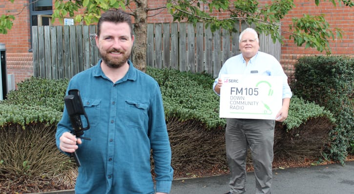 FM105 Recruitment Night PR Photo. One person stood with a mic and another stood with a FM105 sign